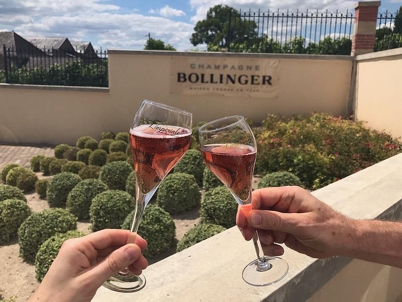 Two glasses of rosé raised in front of the Champagne Bollinger sign
