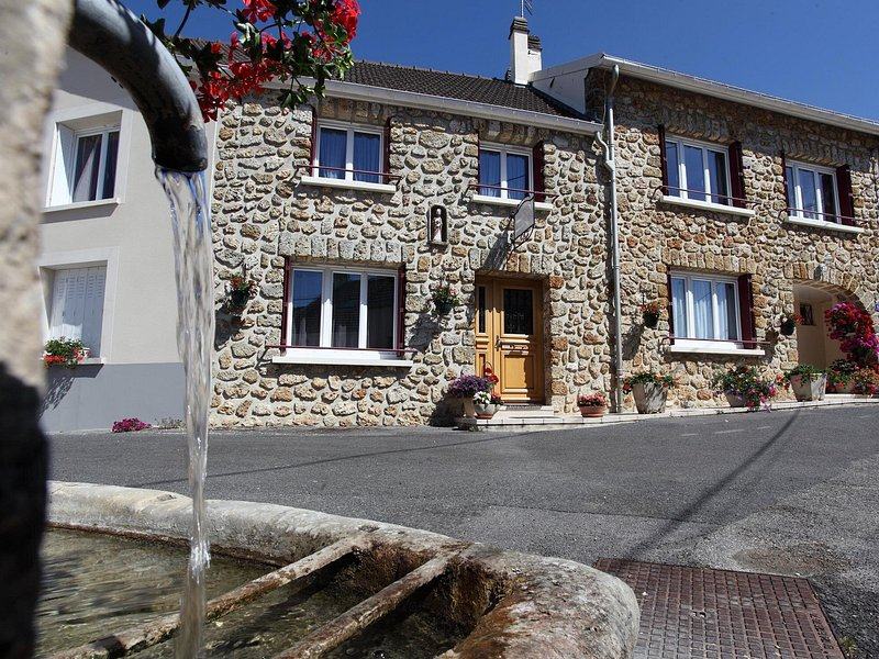 A stone village house with red shutters and window boxes, a fountain running in front